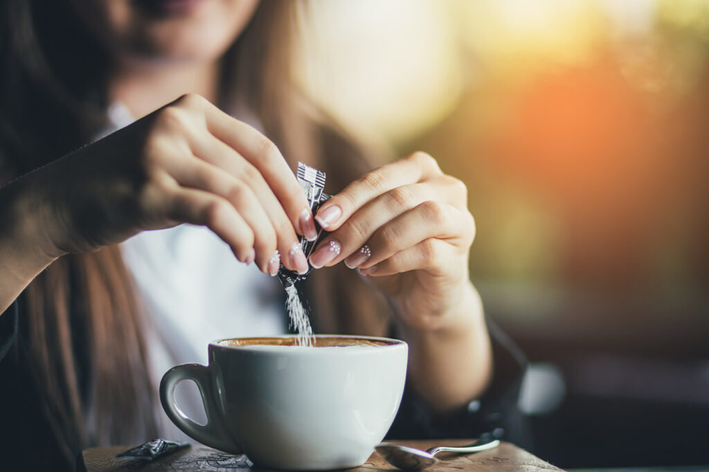 Female hand pours sugar into coffee. 